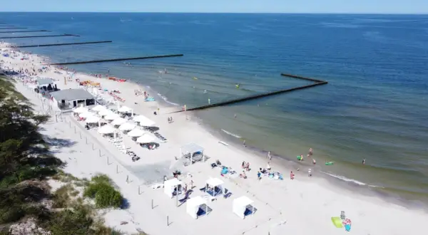 Słoneczny weekend majowy nad morzem. Ludzie odpoczywają na plaży, kąpią się w morzu i opalają pod białymi parasolami.