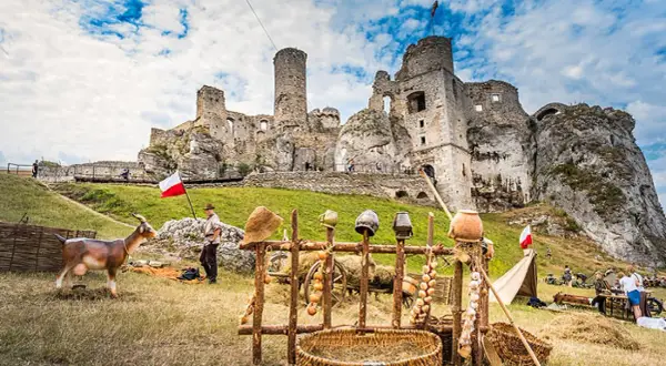 Zamek Ogrodzieniec w całej okazałości, z kozą i historycznymi rekwizytami. Trasa turystyczna zachęca do zwiedzania.