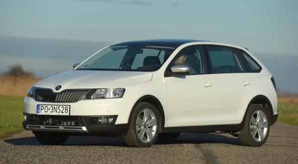 Biała Skoda Rapid z czarnym dachem, z widocznymi światłami i żarówkami, zaparkowana na drodze.