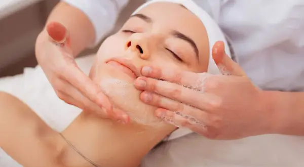 Una donna riceve un trattamento viso con schiuma. Per una pelle luminosa, chiediti ogni quanto fare la pulizia del viso.