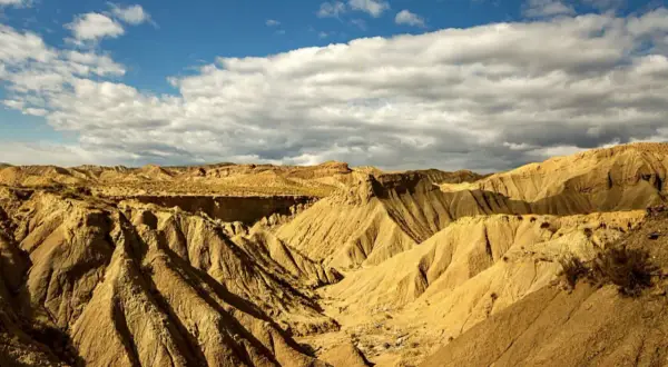 Paisaje árido y erosionado del Desierto de Tabernas, con barrancos y formaciones rocosas bajo un cielo azul con nubes. ¡Un lugar ideal para visitar!