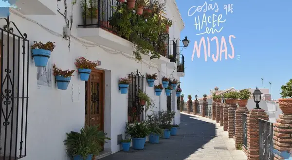 Calle empedrada con casas blancas adornadas con macetas azules y flores. Un camino perfecto para descubrir qué ver en Mijas en una tarde.