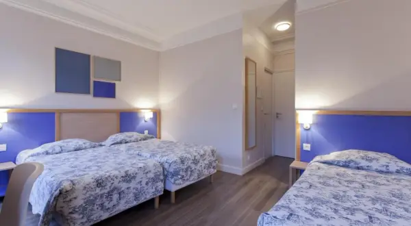 Pokój hotelowy z trzema łóżkami w niebiesko-białą pościelą i niebieskimi zagłówkami.