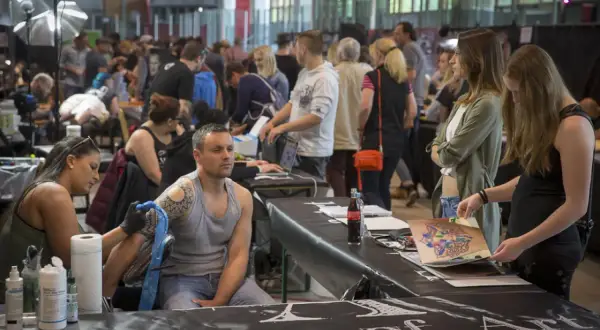 En la convencion tattoo barcelona, un artista tatúa un brazo mientras otros observan diseños.
