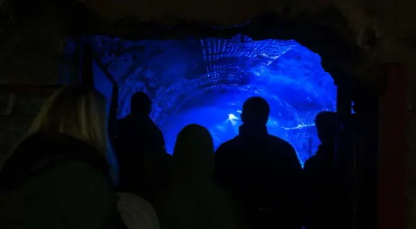 Grupa ludzi wchodzi do sztolni Kowary, gdzie ściany tunelu rozświetla intensywny, niebieski blask.