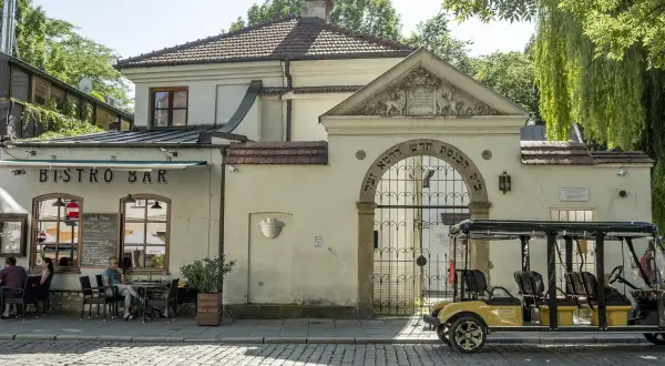 Urokliwy dzień w dzielnicy Kazimierz w Krakowie. Przy bistro barze siedzą ludzie, a obok bramy z hebrajskimi napisami stoi żółty meleks.