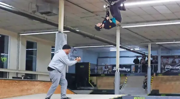 BMX-Fahrer vollführt einen Salto in der Luft in der Wicked Woods Wuppertal. Ein Mann filmt den Stunt.