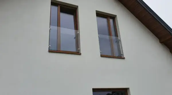 Nowoczesny portfenetr z drewnianymi ramami i szklaną balustradą przy oknach na białej elewacji.