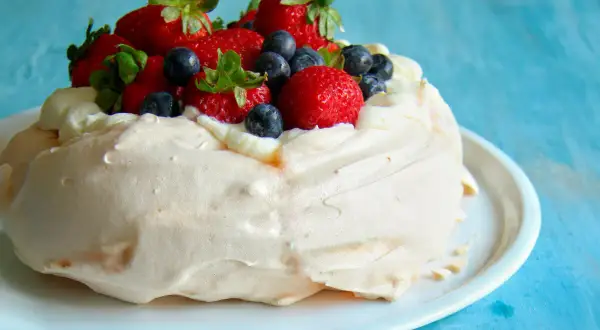Deliciosa pavlova receta original, coronada con fresas y arándanos frescos, sobre una base de merengue crujiente y crema batida.