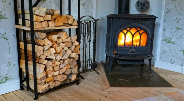 En mysig brasa sprakar i en gjutjärnskamin. Bredvid står en hylla fylld med ved, redo att installera braskamin för värme och trivsel.