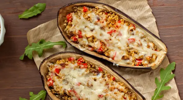 Dos mitades de berenjenas rellenas con cuscús, pimientos y queso derretido, cocinadas en airfryer.