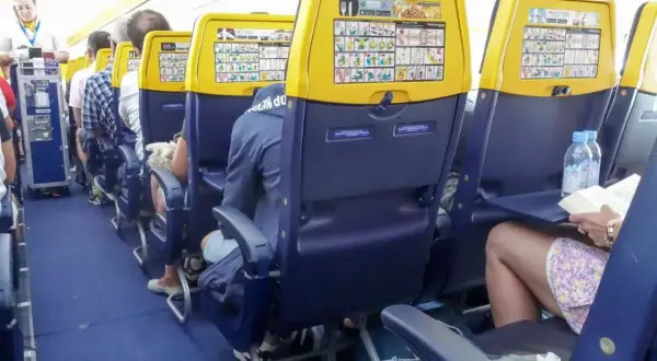 Wnętrze samolotu Ryanair. Widok na rząd siedzeń z żółtymi zagłówkami i instrukcjami bezpieczeństwa. Numeracja miejsc w samolocie Ryanair jest widoczna.