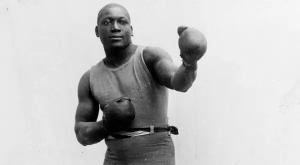 A boxer in an old boxing stance, wearing a tank top and shorts, with gloves on both hands, ready to fight.