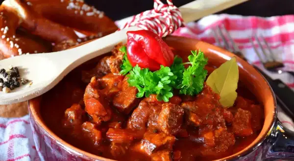 Pyszny gulasz wołowy w glinianej misce, ozdobiony papryczką chili i natką pietruszki. Idealny przepis, jak zrobić gulasz, by zachwycić bliskich.