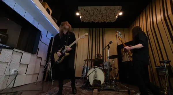 Zakk Cervini and his band rock out in a studio, with a guitarist in the foreground, a bassist to the right, and a drummer in the background.