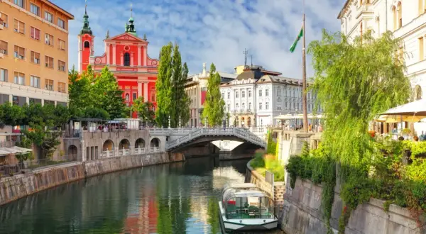 Lublana atrakcje: rzeka Ljubljanica, Most Potrójny, kościół Franciszkanów i łódź wycieczkowa.