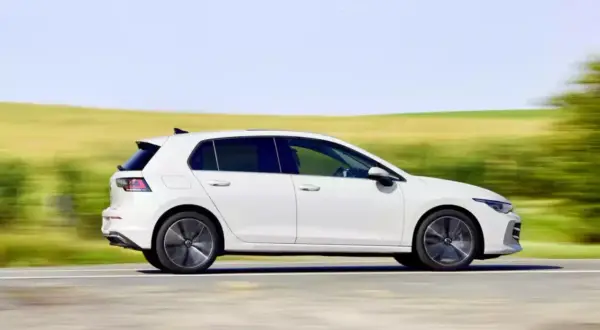 Biały hatchback pędzi po drodze, otoczony rozmytymi zielonymi polami i błękitnym niebem.