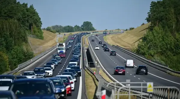 Długi korek samochodów na autostradzie A6. Wiele pojazdów stoi w powolnym ruchu, otoczonych zielenią drzew.
