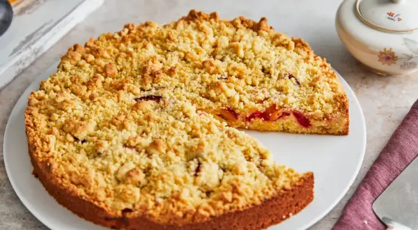 Ein saftiger Streuselkuchen mit Obst, bedeckt mit goldbraunen Streuseln, wartet darauf, angeschnitten zu werden.