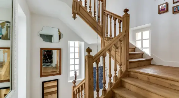Un bel escalier en bois, prêt à être nettoyé. Des miroirs et des cadres photo décorent le mur blanc.