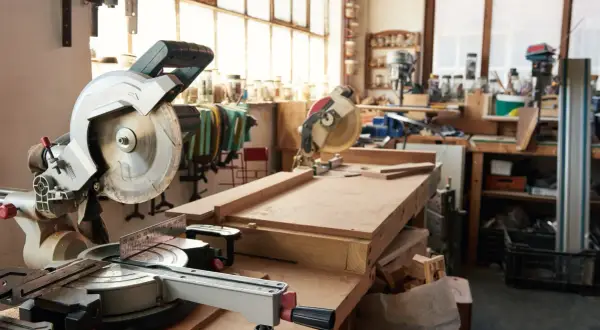 Un atelier menuiserie maison avec des scies circulaires, des établis et des outils. Des planches de bois sont prêtes pour être travaillées.
