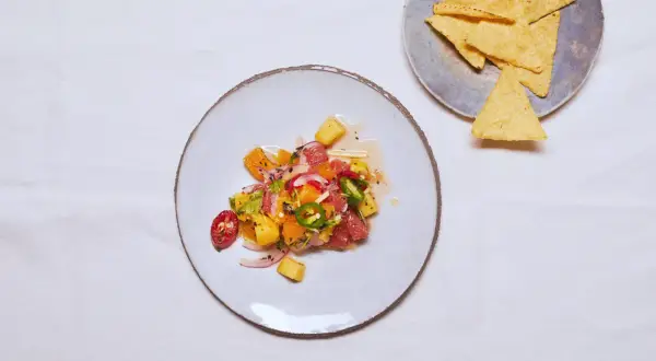 Kolorowe ceviche z owocami cytrusowymi, ananasem, papryczką chili i czerwoną cebulą, podane na talerzu obok nachos.