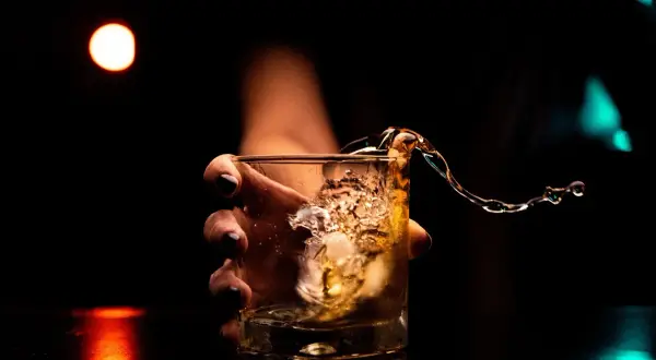 Dłoń trzyma szklankę z whisky, gdy płyn rozlewa się, tworząc falę. Kto wydaje koncesję na alkohol, by móc cieszyć się takimi chwilami?