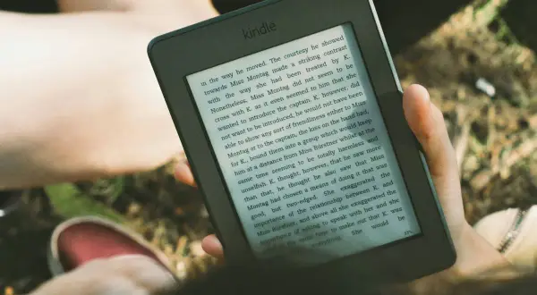 Osoba czyta książkę na czytniku Kindle, korzystając z Legimi.