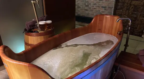 Entspannendes Bier-Wellness-Erlebnis in Tschechien: Ein hölzerner Bottich gefüllt mit schäumendem Bier, daneben ein Zapfhahn und zwei Biergläser.