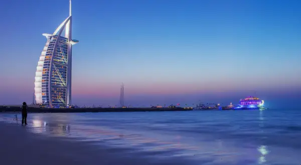 Wieżowiec Burdż al-Arab i oświetlony statek na tle nocnego nieba nad Zatoką Perską.