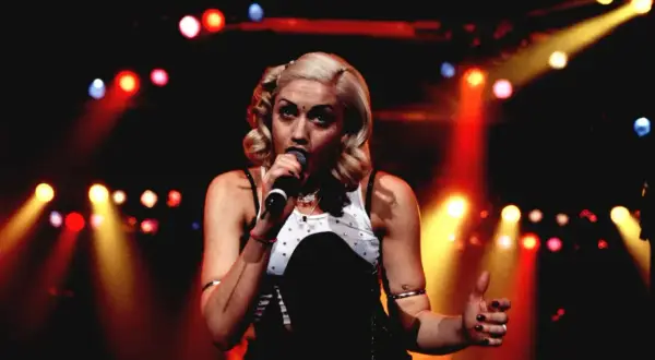 Gwen Stefani śpiewa na scenie, otoczona kolorowymi światłami.