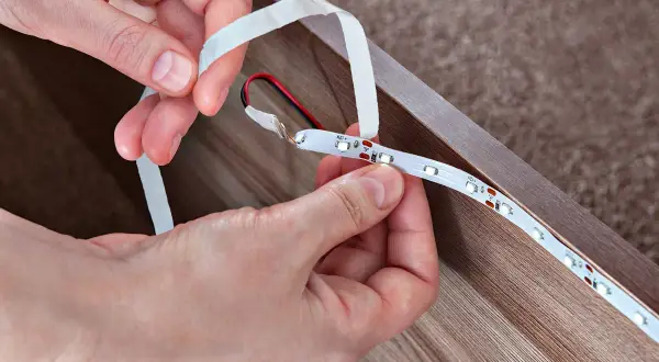 Dłonie łączą taśmy LED RGB, przygotowując je do montażu. Prosty sposób na stworzenie nastrojowego oświetlenia.