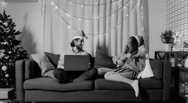 Wśród nocnej ciszy chwyty ukulele i śmiech przy laptopie. Para w czapkach Mikołaja cieszy się świąteczną atmosferą.