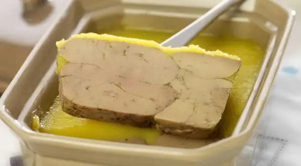Tranche de foie gras au porto blanc, servie dans un plat en céramique avec une cuillère.