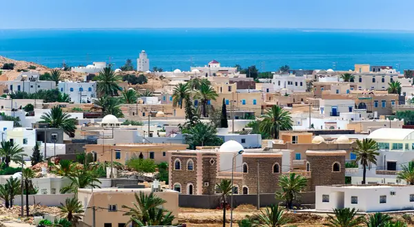 Piękne, białe domy z niebieskimi okiennicami i palmami na tle błękitnego morza. Idealna pogoda Djerba.