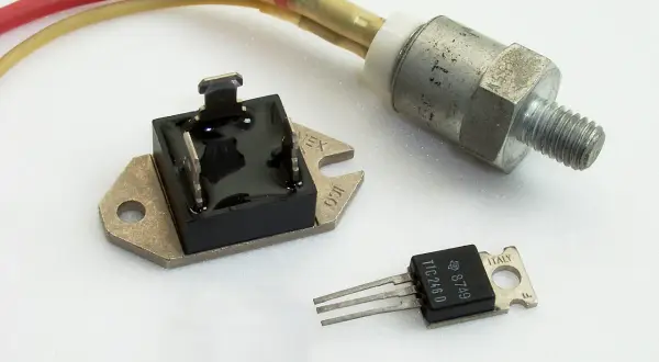 Trzy elementy elektroniczne: mostek prostowniczy, tranzystor TIC246D i metalowy element z gwintem, prawdopodobnie regulator napięcia.