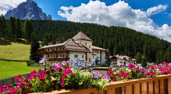 Fiori colorati su un balcone con vista su un hotel e le montagne, un'oasi di pace nei rifugi Val Gardena.
