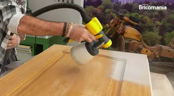 Hombre pintando una puerta de madera con una pistola pulverizadora. El resultado es un acabado liso y uniforme.
