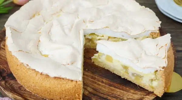 Ein saftiger Rhabarberkuchen mit Baiserhaube, ein Stück davon ist angeschnitten und zeigt die cremige Füllung.