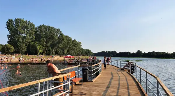 Ludzie odpoczywają i kąpią się nad zalewem Borki Radom. Drewniane molo zaprasza do spacerów i podziwiania widoków.