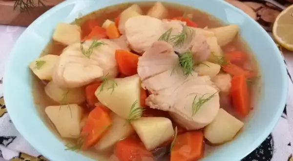 Miska zupy rybnej z kawałkami ryby, ziemniaków i marchewki, udekorowana koperkiem.