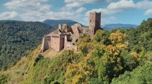 Les 3 châteaux de Ribeauvillé, perchés sur une colline boisée, se dressent fièrement sous un ciel bleu parsemé de nuages.