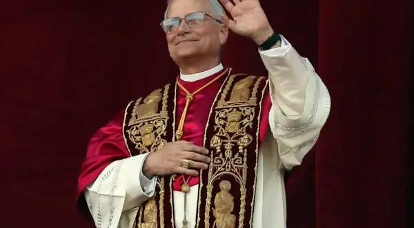 Papież w bogato zdobionej szacie pozdrawia wiernych. Jego uśmiech i gest ręki budzą nadzieję, a jego strój przypomina o tym, skąd pochodzi papież i jego dziedzictwo.