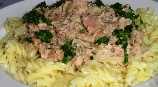 Pyszny makaron z tuńczykiem, posypany świeżą natką pietruszki, podany na białym talerzu.