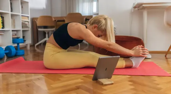 Kobieta ćwiczy w domu, sprawdzając na tablecie, czy trening siłowy spala tłuszcz. Obok leżą hantle.