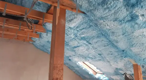 Piana na poddasze tworzy izolacyjną warstwę na drewnianej konstrukcji dachu, z widocznym oknem dachowym.