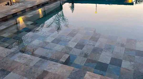 Escalones de baldosas de piedra entran en unas piscinas interiores, reflejando luces y árboles.