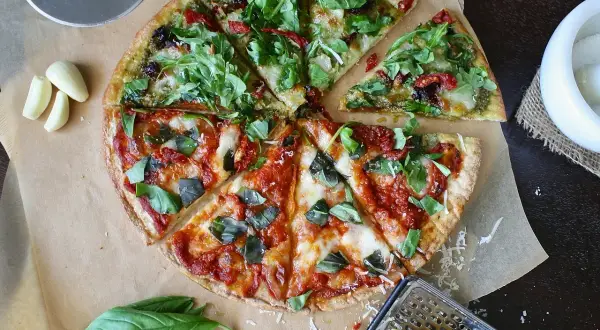 Pizza podzielona na pół: jedna połowa z pesto i rukolą, druga z sosem pomidorowym i bazylią.
