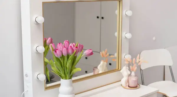 Eleganckie lustro makijażowe z żarówkami, ozdobione bukietem różowych tulipanów i świecami. Idealne do porannego rytuału.
