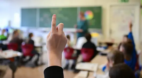 Ein Schüler hebt die Hand im Unterricht. Seit wann gibt es die Schulpflicht in Deutschland? Die Antwort liegt im Dunkel der Geschichte, aber die heutige Schulpflicht ist ein Meilenstein.